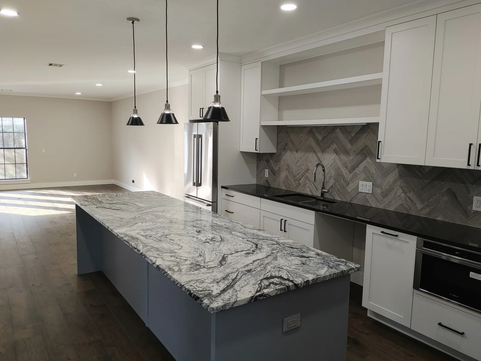 Modern kitchen with white cabinets, waterfall granite island, herringbone backsplash, and black pendant lights