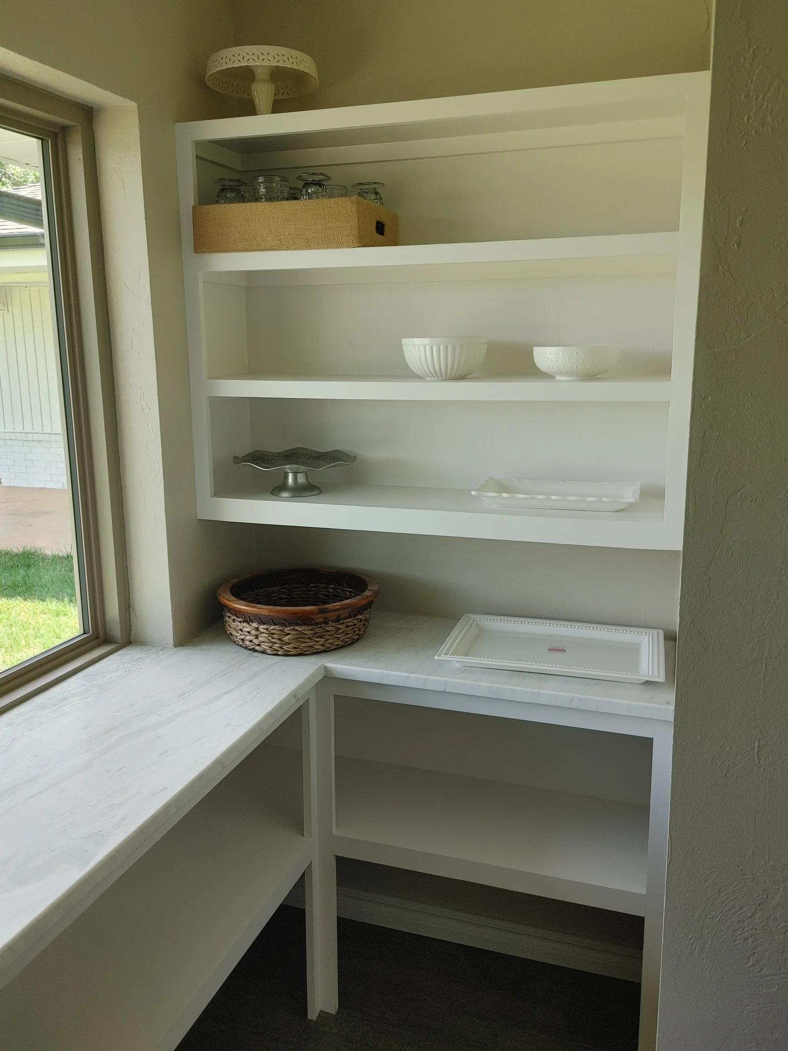 White built-in pantry shelving with four open shelves, marble countertop, and lower storage compartment