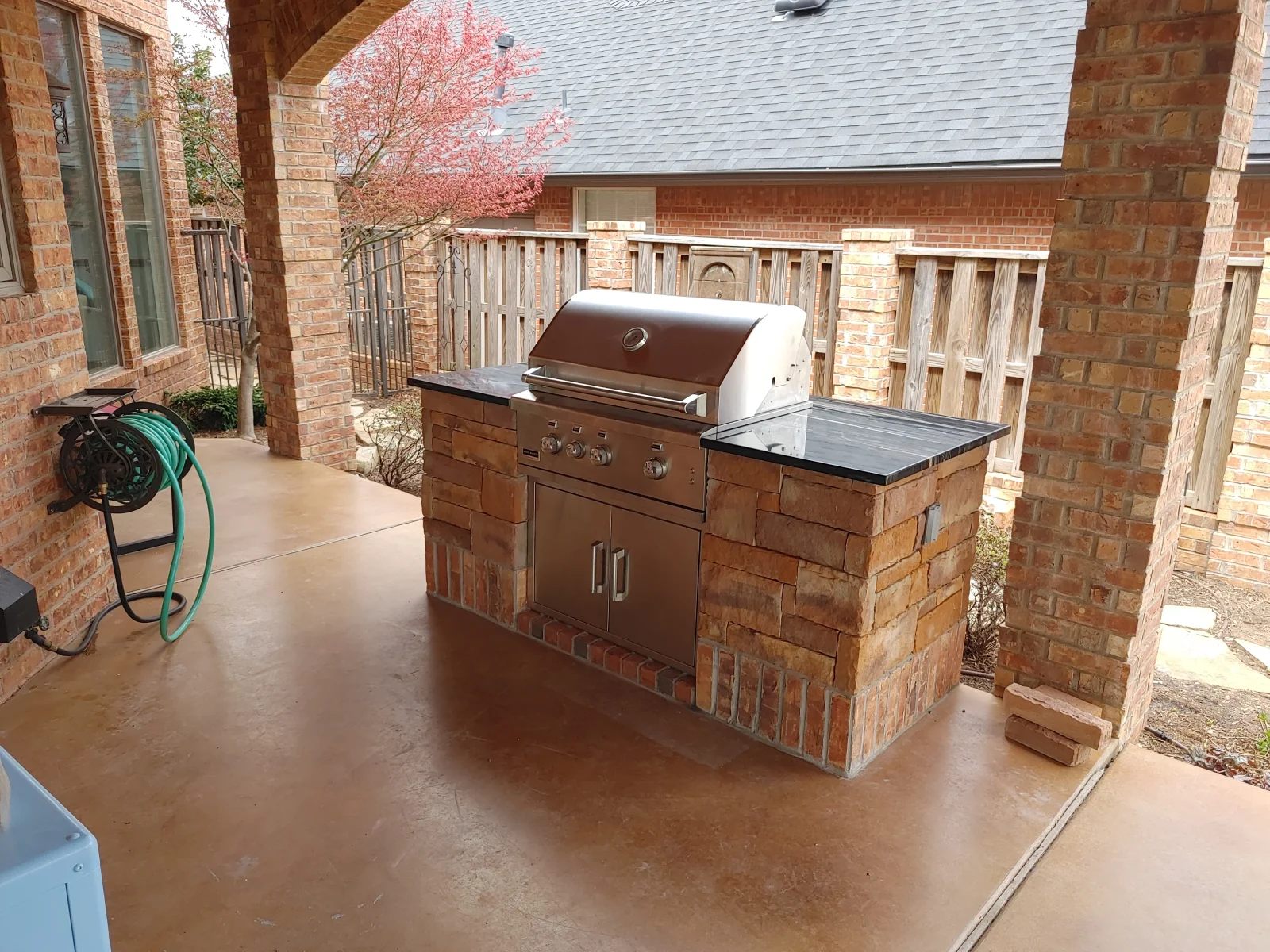 Brick grill island with stainless steel grill and granite countertop on concrete patio