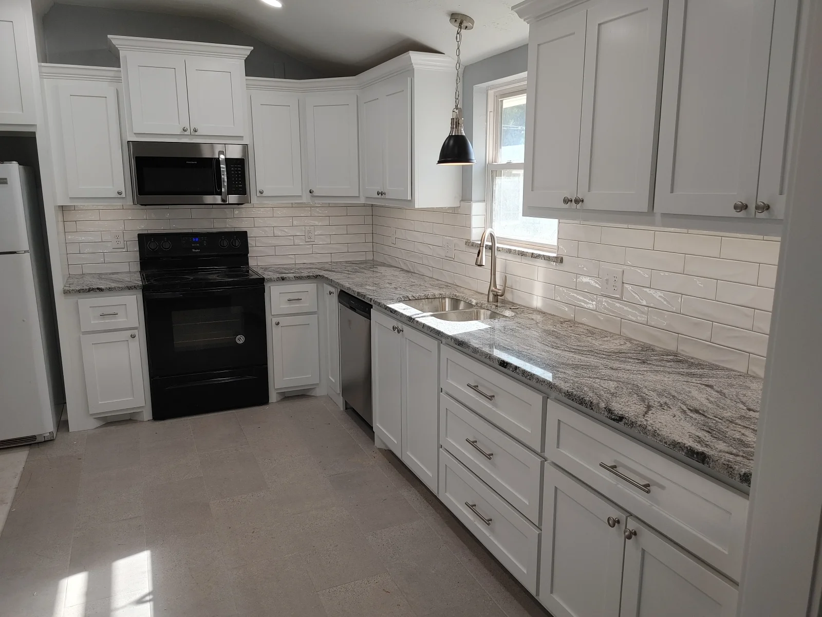 White kitchen with granite counters, subway tile backsplash, and black appliances