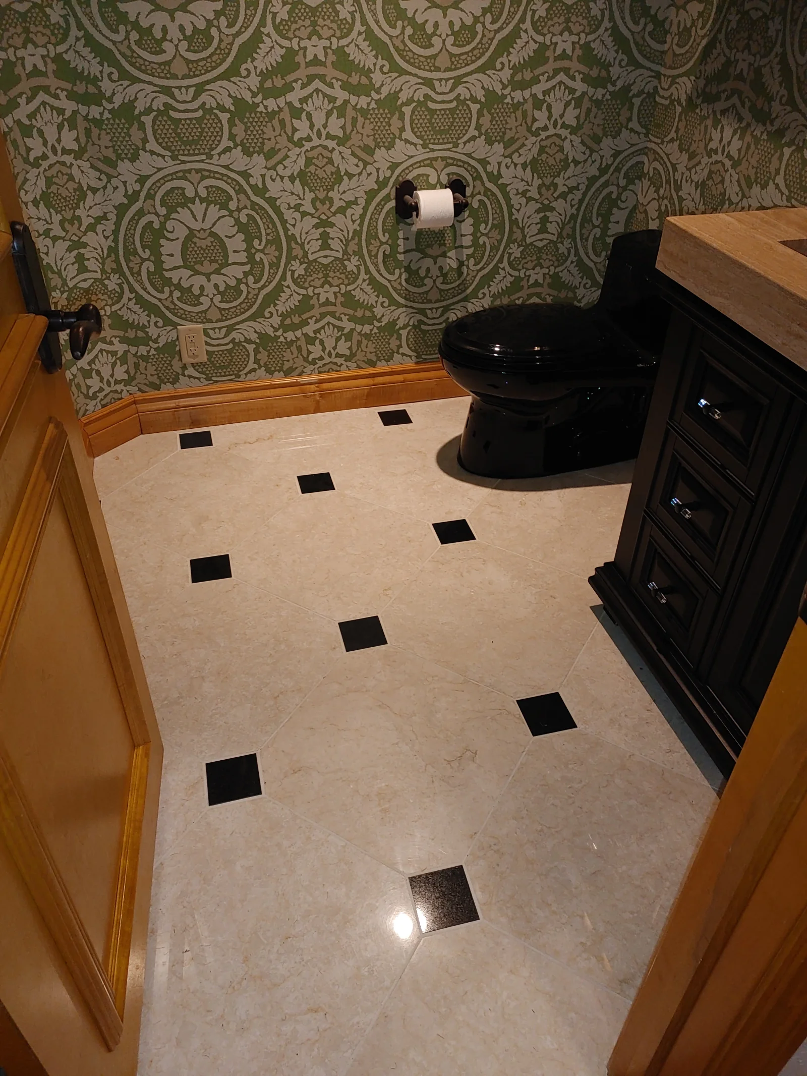 Marble floor with black slate inlays, green damask wallpaper, black toilet, wood vanity