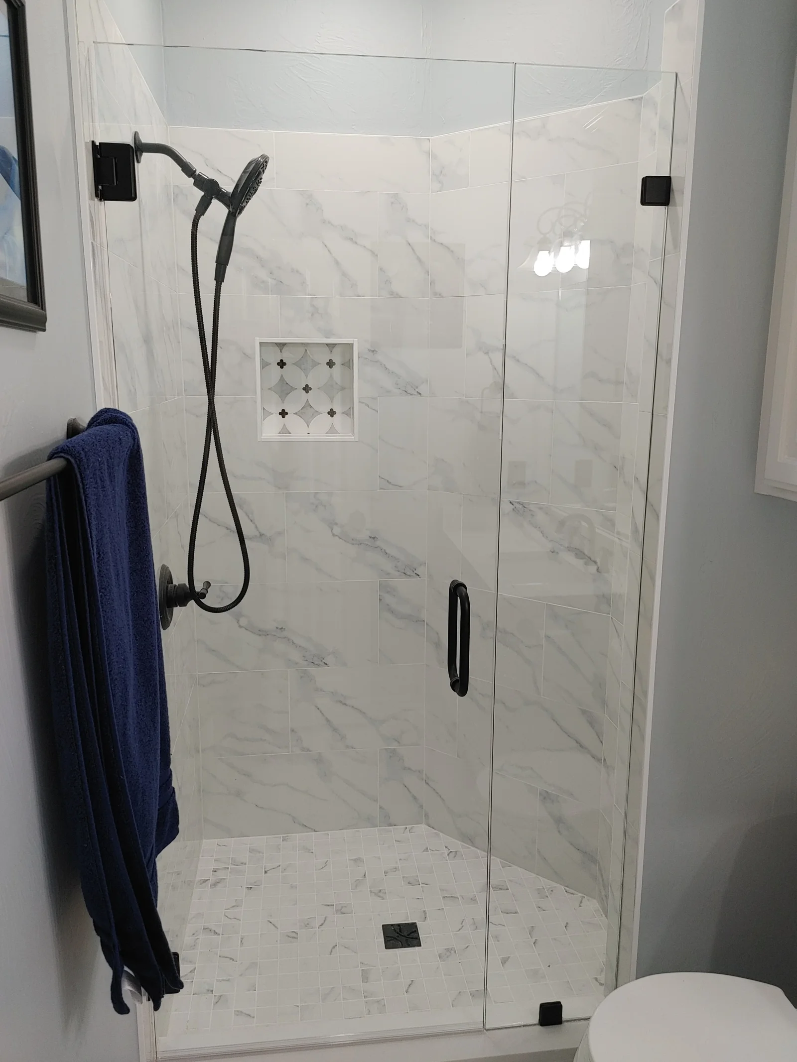 Marble tile shower with frameless glass enclosure, rainfall showerhead, and mosaic floor