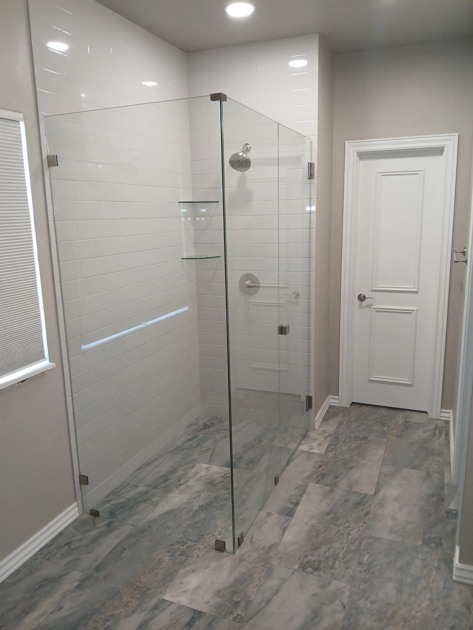 Frameless glass shower with white subway tile walls and gray marble floor tile