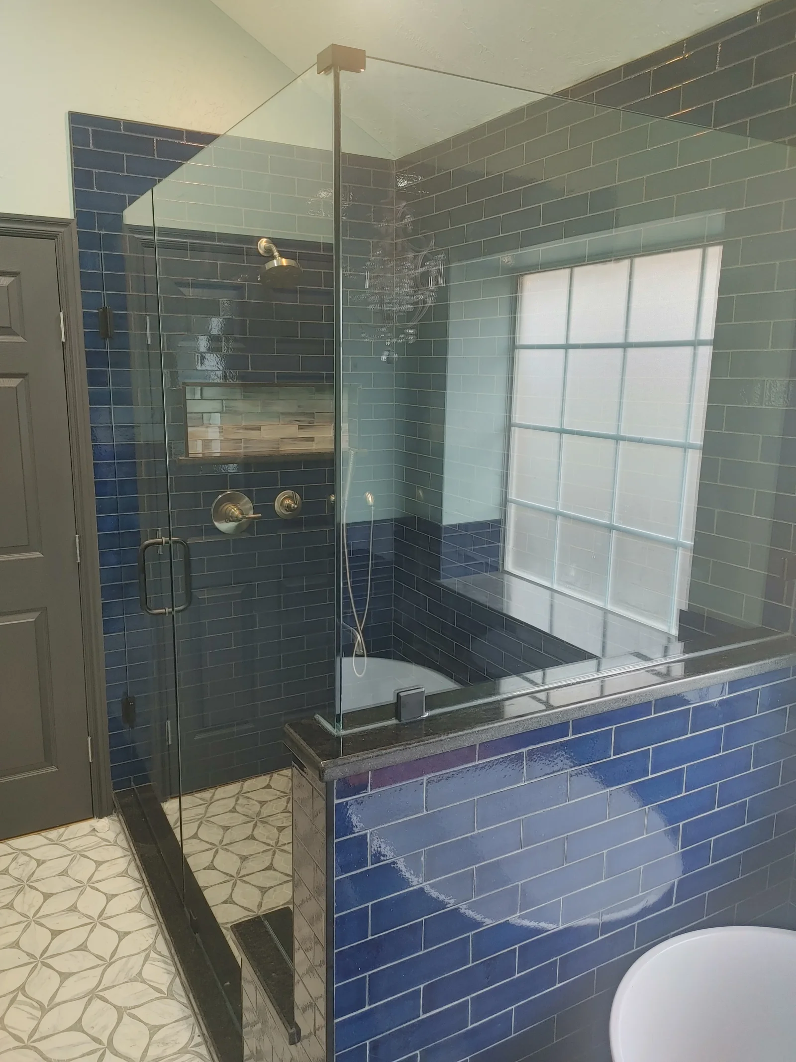 Frameless glass shower enclosure with dark subway tile walls and polished nickel fixtures