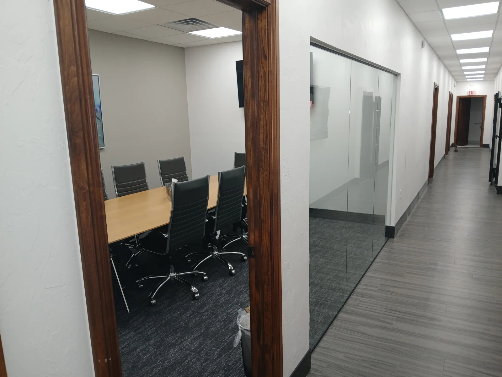 Commercial office interior with glass partition walls, wood frames, drywall, and concrete flooring