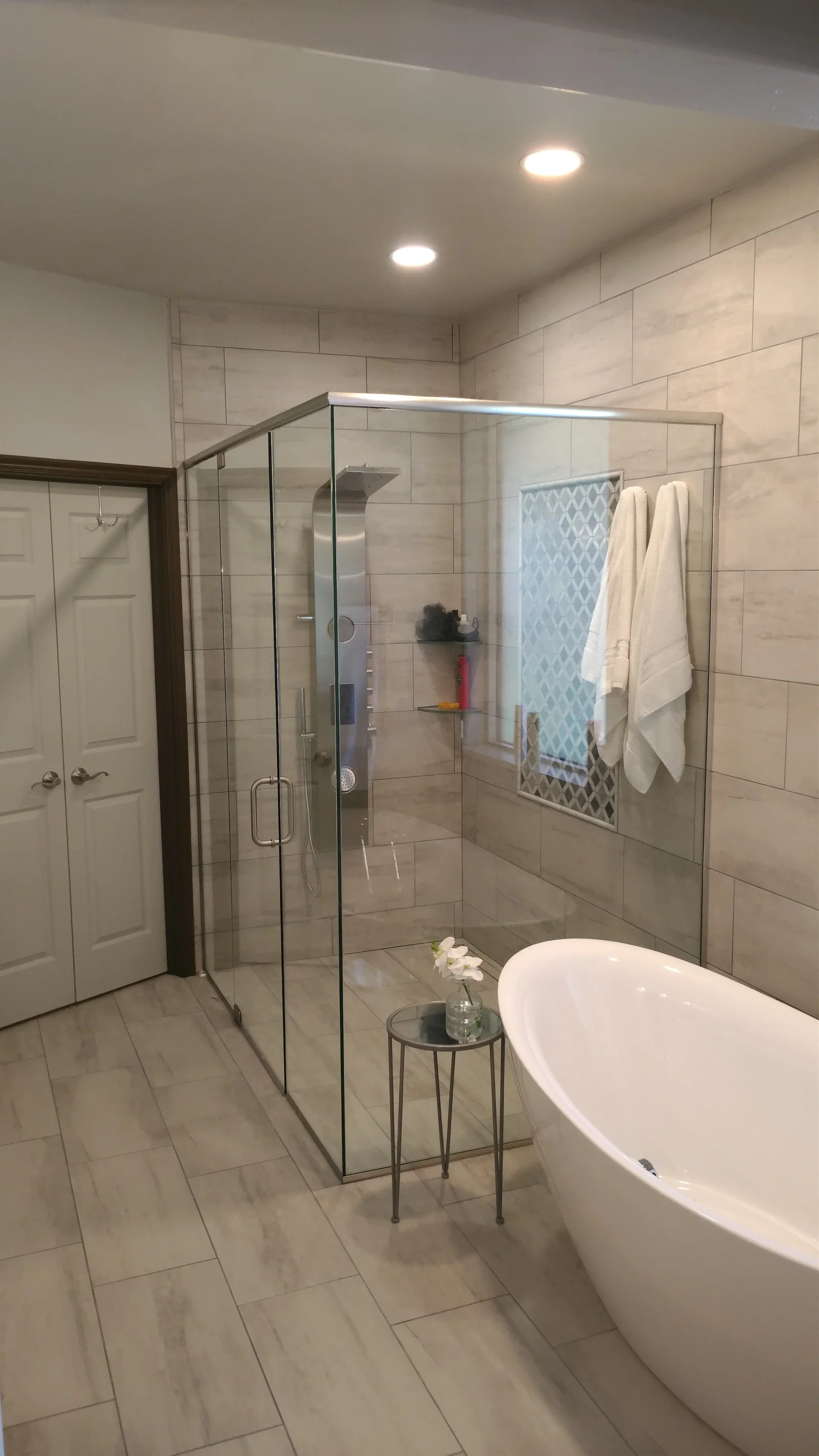 Modern bathroom with frameless glass shower, freestanding tub, and neutral tile throughout