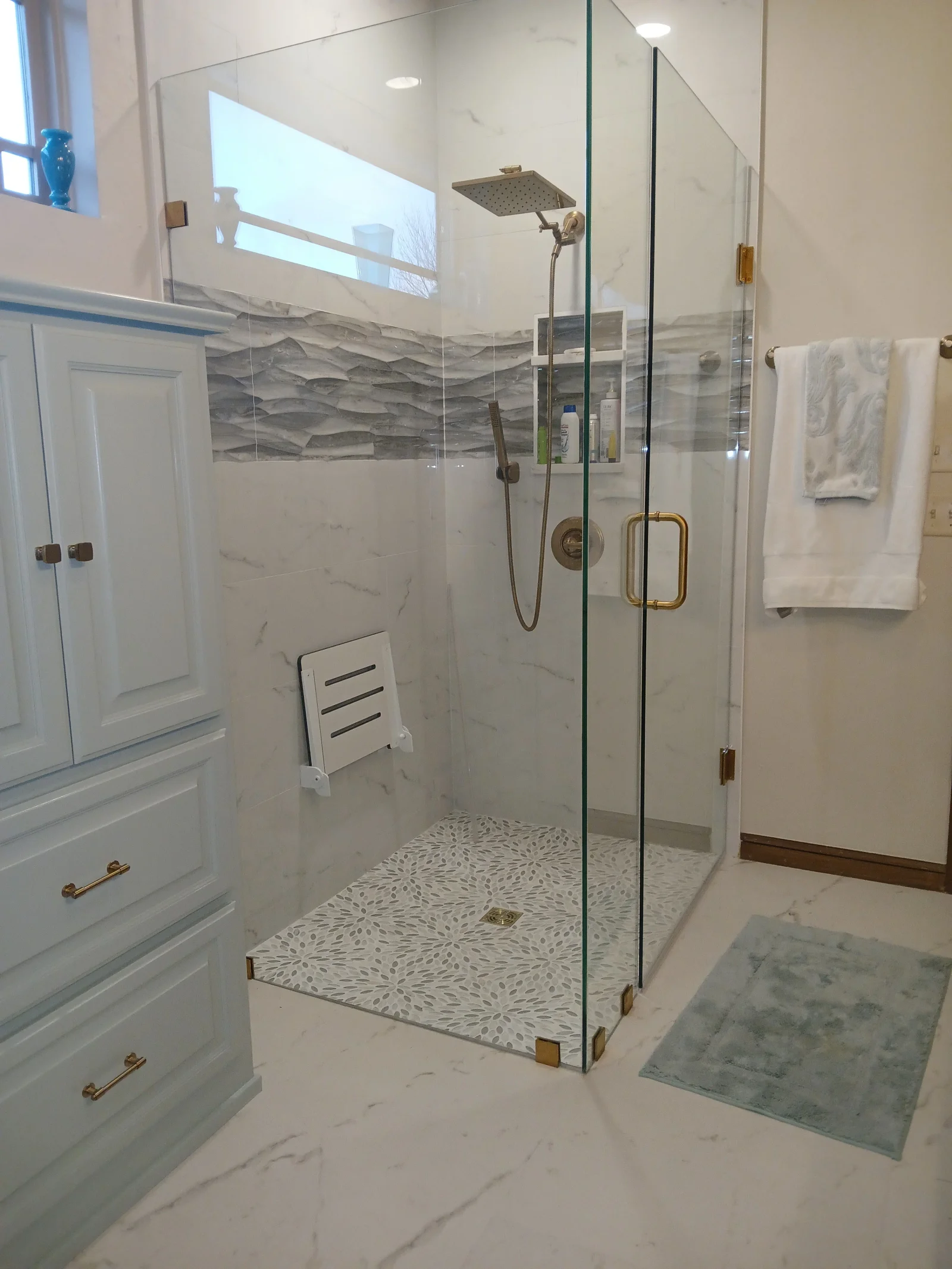 Frameless glass shower with marble tile, white vanity, and brass fixtures in modern bathroom