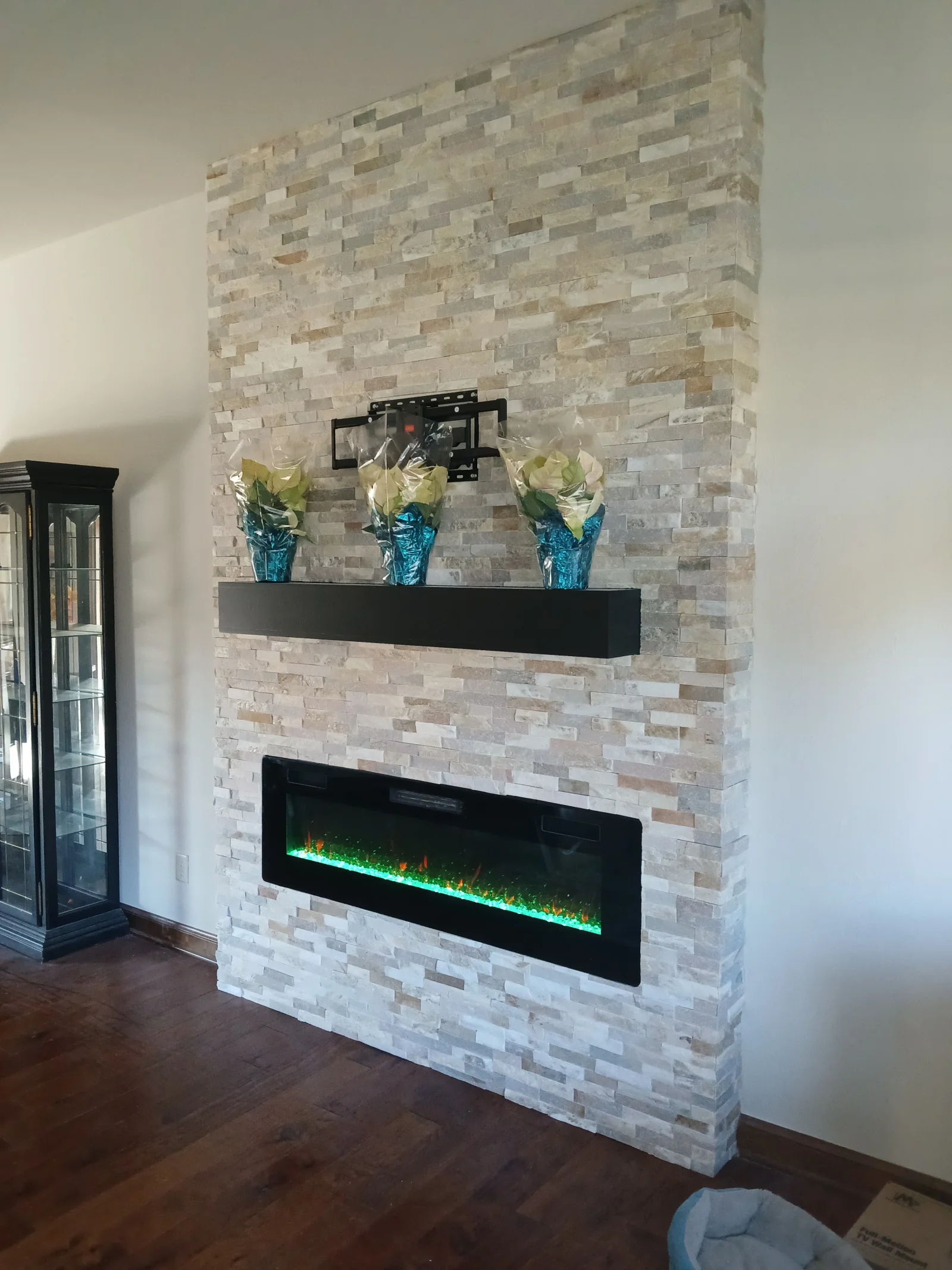 Stacked stone veneer fireplace wall with electric insert and floating shelf