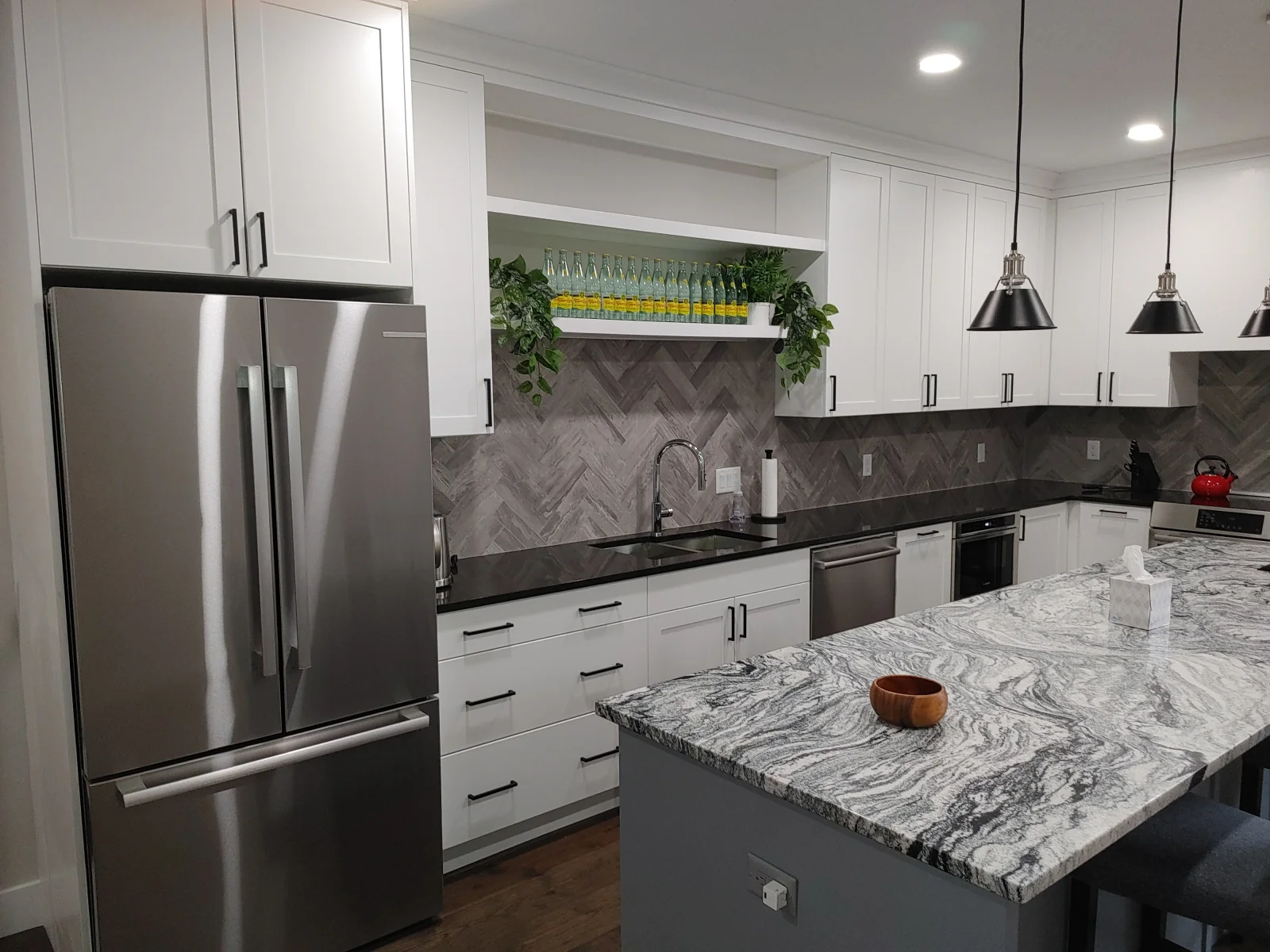 White kitchen with marble island, herringbone backsplash, stainless steel appliances