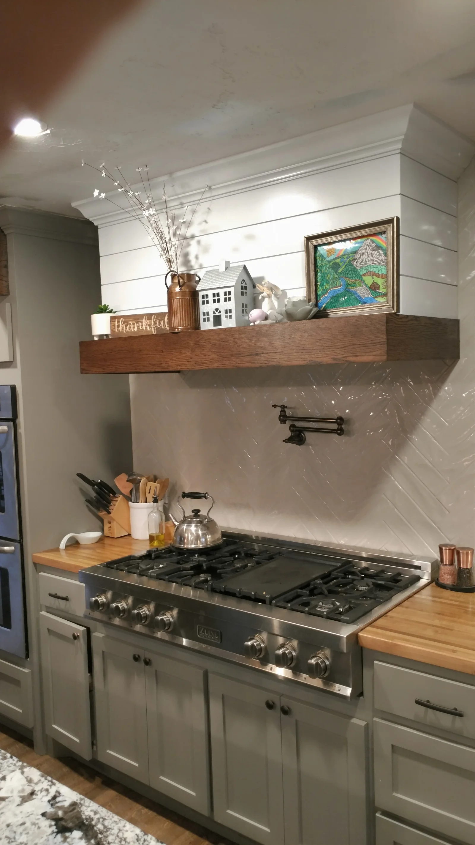 White kitchen with shiplap backsplash, gas range, floating wood shelf, and shaker cabinets