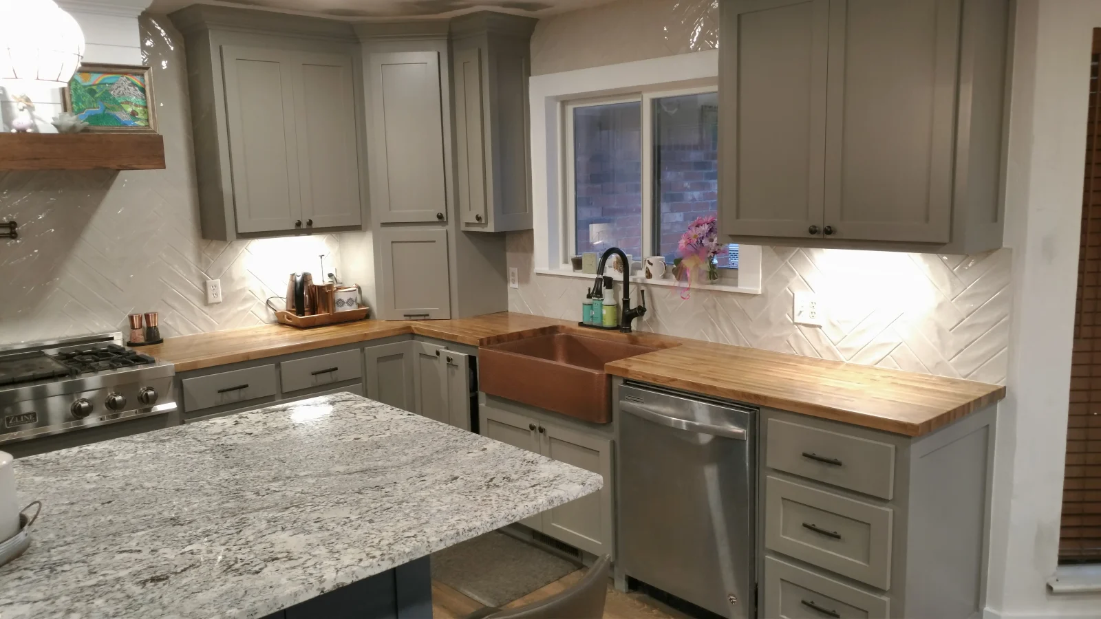 Gray shaker cabinets, herringbone subway tile, wood and quartz countertops, copper farmhouse sink