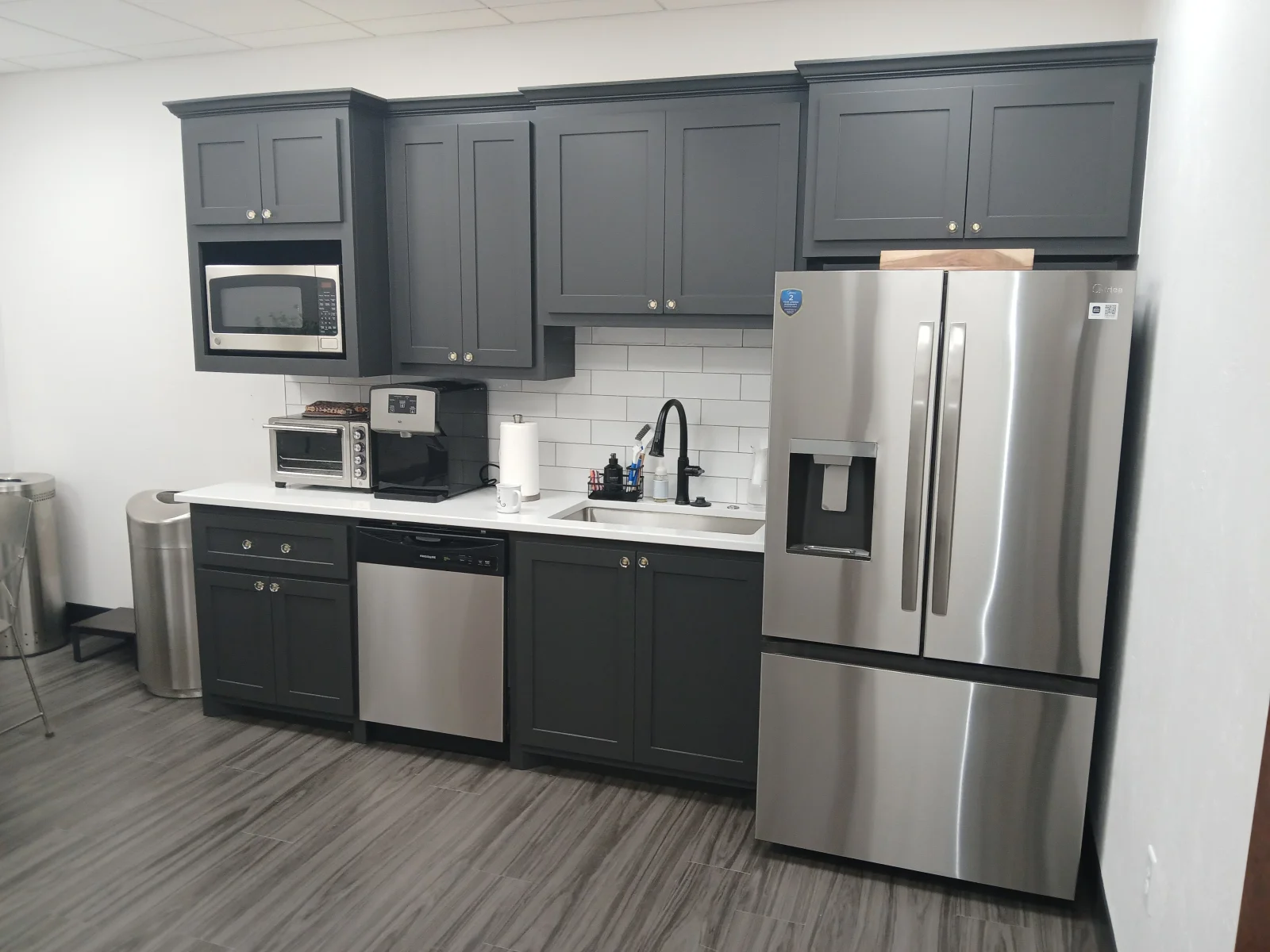Two-tone kitchen with gray cabinetry, stainless steel appliances, white countertops, and subway tile backsplash