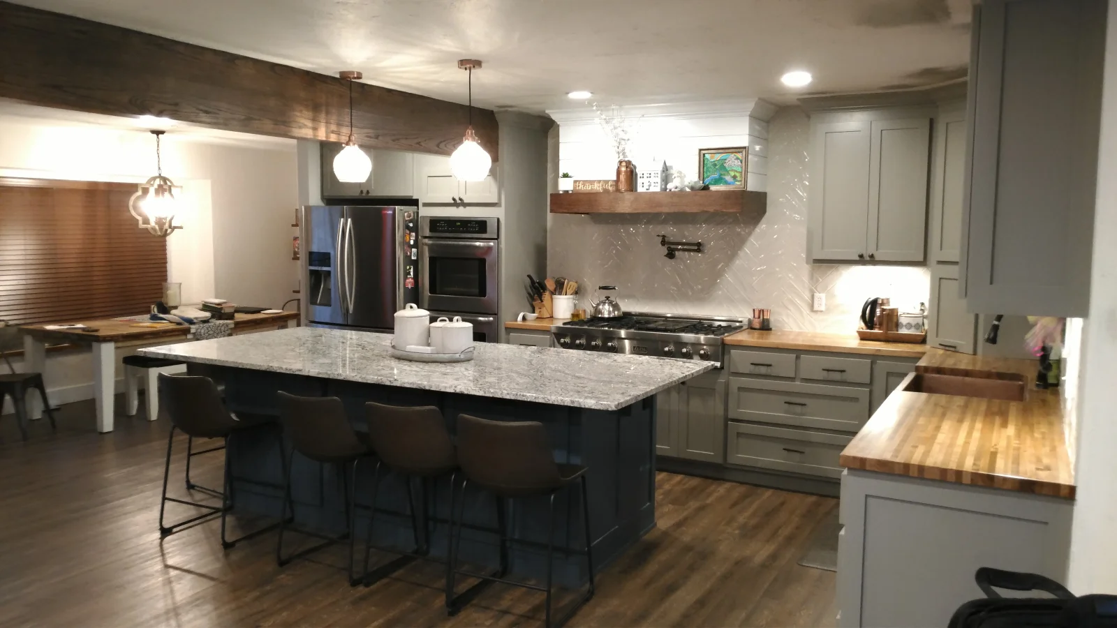 Modern kitchen with gray cabinetry, navy island, quartz counters, stainless appliances, and pendant lights